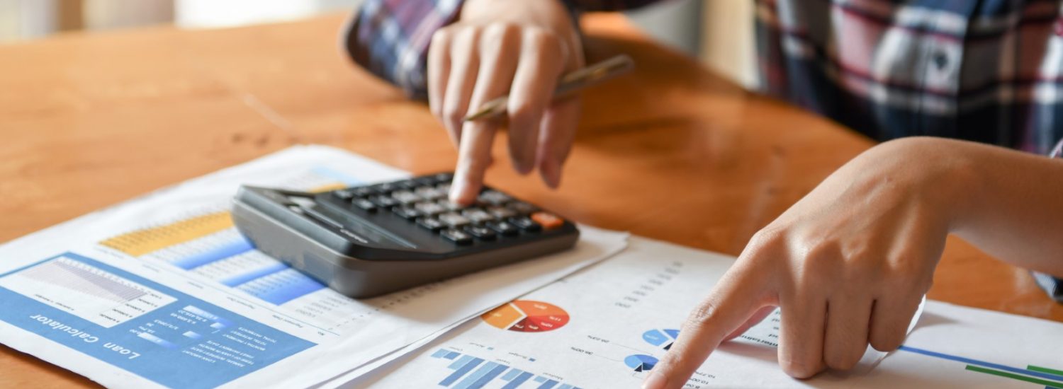 Hand pointer at graph and other hand hold pen and presses the calculator.