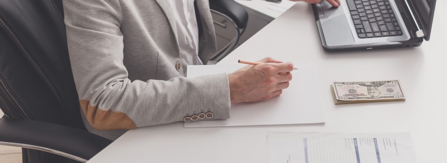 A male accountant works at a pc in an office at home. Payroll and cash withdrawal